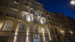 Un immeuble à plusieurs étages, doté de balcons et de fenêtres en arc de cercle, avec un commerce fermé au rez-de-chaussée.