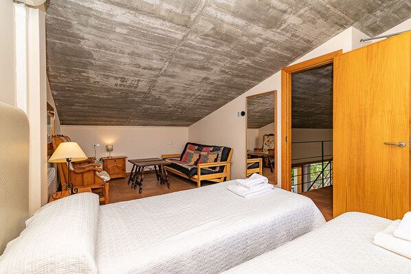 A room with a bed, a sofa, a table, and a chair. There is a wooden door and a window.