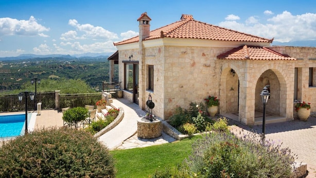 A stone building with a tiled roof, a swimming pool, and a view of the countryside.