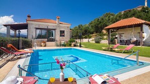 A swimming pool with lounge chairs, a small building with a stone facade, and a view of the surrounding landscape.