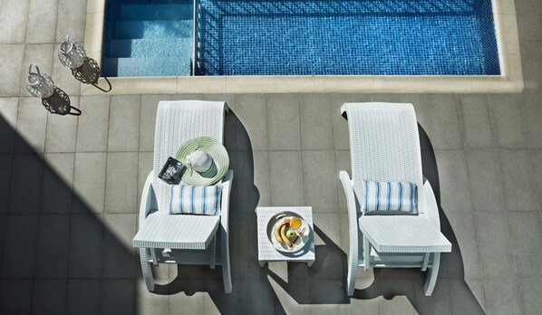 Zwei Lounge-Stühle, Sonnenliegen, ein kleiner Tisch mit Obstplatte und zwei dekorative Laternen am Pool.