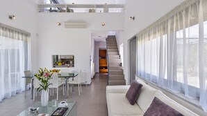Un salon moderne avec une table basse en verre, un canapé blanc et un coin repas comprenant une table et des chaises en verre.