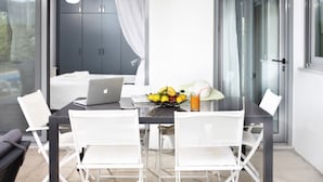 Un espace repas moderne avec une table en verre, des chaises blanches, un ordinateur portable, un panier de fruits et un verre de jus d’orange.