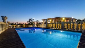 Una piscina con bordo in legno, un'area salotto coperta e un recinto decorativo.