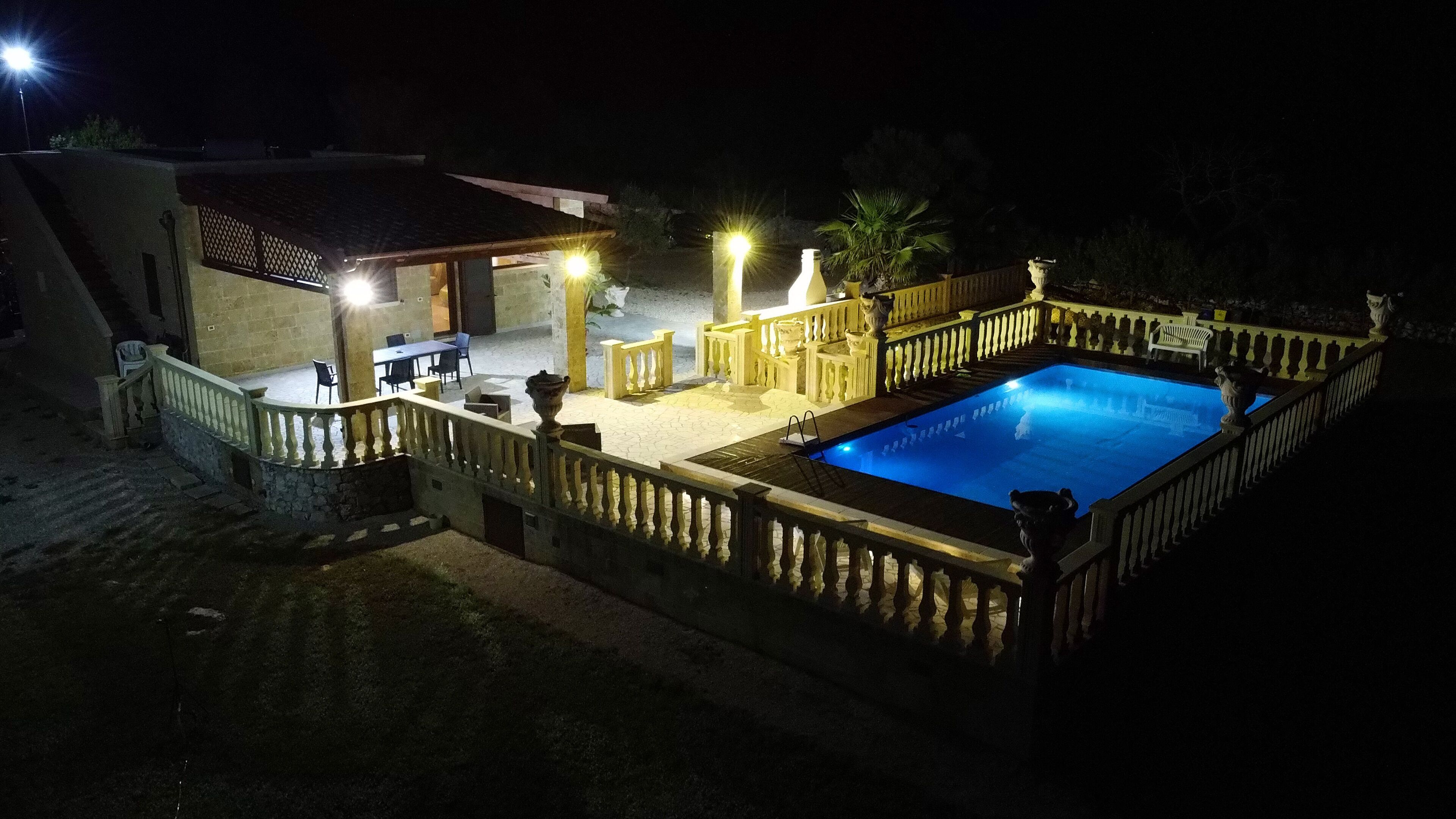 A swimming pool with a wooden deck and railing, surrounded by a building with outdoor seating and a covered area.