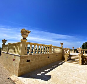 Un chemin de pierre menant à un escalier agrémenté de balustrades et de vases décoratifs.
