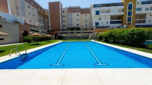 A swimming pool with two lanes, surrounded by a well-maintained lawn and a row of multi-story buildings. - OLIMPO PENTHOUSE WITH SEA VIEWS 5 MINUTES FROM THE BEACH. (Málaga)