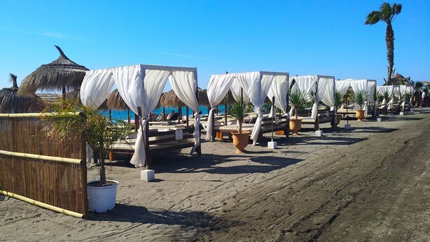 A beachside resort with thatched-roof huts, white canopies, and potted plants. - OLIMPO PENTHOUSE WITH SEA VIEWS 5 MINUTES FROM THE BEACH. (Málaga)