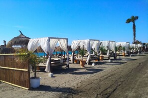 Un complexe hôtelier en bord de mer, avec des bungalows aux toits de chaume, des auvents blancs et des plantes en pot.