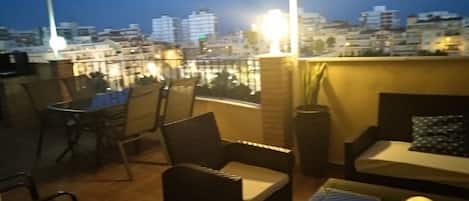 Una terraza en la azotea con mobiliario exterior, vistas de la ciudad y un muro de ladrillo.