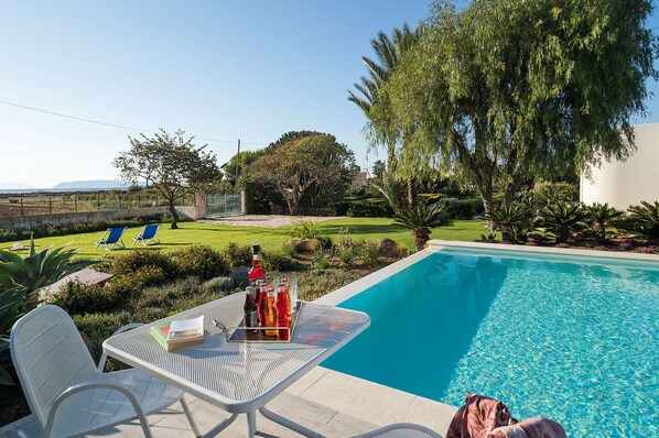 A poolside area with a table set for drinks, a chair, and a dog. - Villa with pool, 450 metres from sea, near Trapani, Sicily - 14 pax (Paceco)