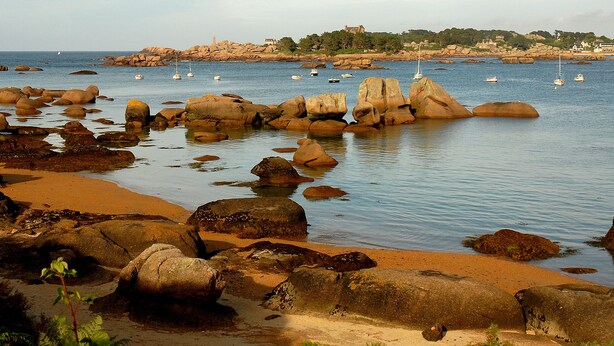 A rocky beach with large boulders and calm water.