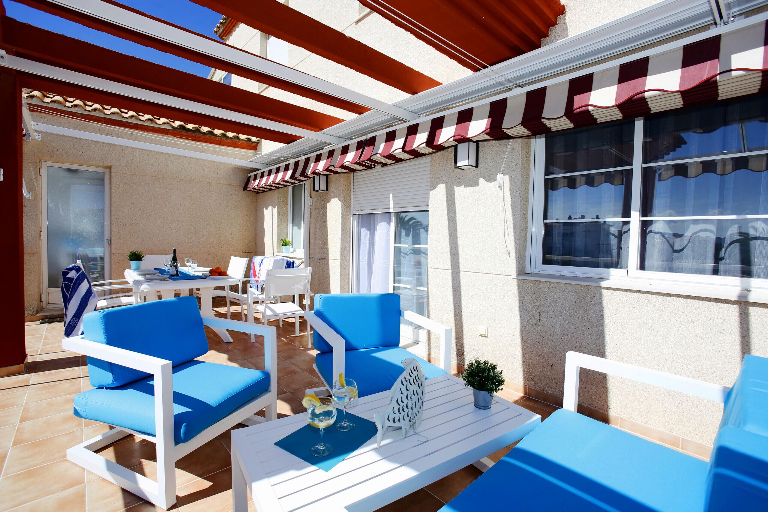 An outdoor seating area with blue and white furniture, a table with drinks, and a striped awning.