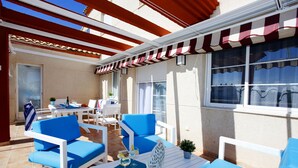 An outdoor seating area with blue and white furniture, a table with drinks, and a striped awning. - 177 Maravista (Denia)