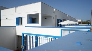 Un edificio moderno con paredes blancas y detalles azules, que cuenta con una entrada protegida por una reja y un área de estar al aire libre techada.