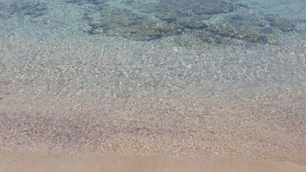 Una playa con aguas transparentes y poco profundas, y una línea de costa distante.