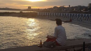 Una persona sentada junto a la orilla al atardecer.