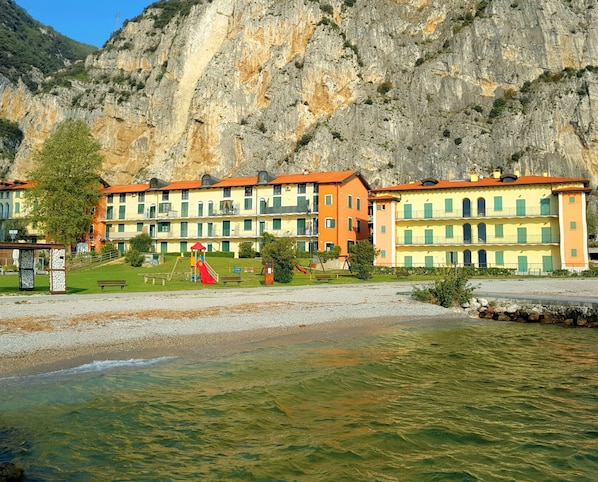 A coastal hotel with multiple balconies, a playground, and a rocky cliff backdrop.
