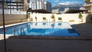 En rektangulär swimmingpool med en metallstege på ena sidan, omgiven av en kakelbeklädd poolterrass.