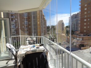 En balkon med et bord, en stol og udsigt til omkringliggende bygninger.