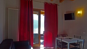 Ein Zimmer mit Balkon, roten Vorhängen, einem weißen Tisch mit Stühlen, einem Fernseher an der Wand und einer Heizung.