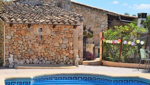 Un bâtiment en pierre avec un toit recouvert de tuiles, une piscine aux carreaux de mosaïque bleus et des décorations colorées.