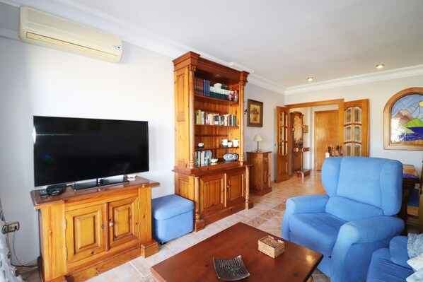 A living room with a television, wooden bookshelves, a blue armchair, and a coffee table.