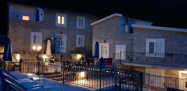Un bâtiment en pierre doté de nombreuses fenêtres, d’un balcon et d’un espace extérieur aménagé avec des parasols.
