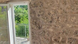 A room with a stone wall, a wooden beam ceiling, and a window with a view of greenery outside. -  Hillside apartment with stunning views of sea and mountains, sea 2 km, pool (Tivat)