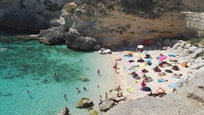 Una playa con agua turquesa cristalina, formaciones rocosas y gente tomando el sol y nadando.