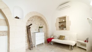 Una habitación con pared de piedra, muebles blancos y una pequeña estantería con adornos.