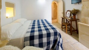 Un dormitorio con cama, una colcha a cuadros, un escritorio con silla, televisor y aire acondicionado instalado en la pared.