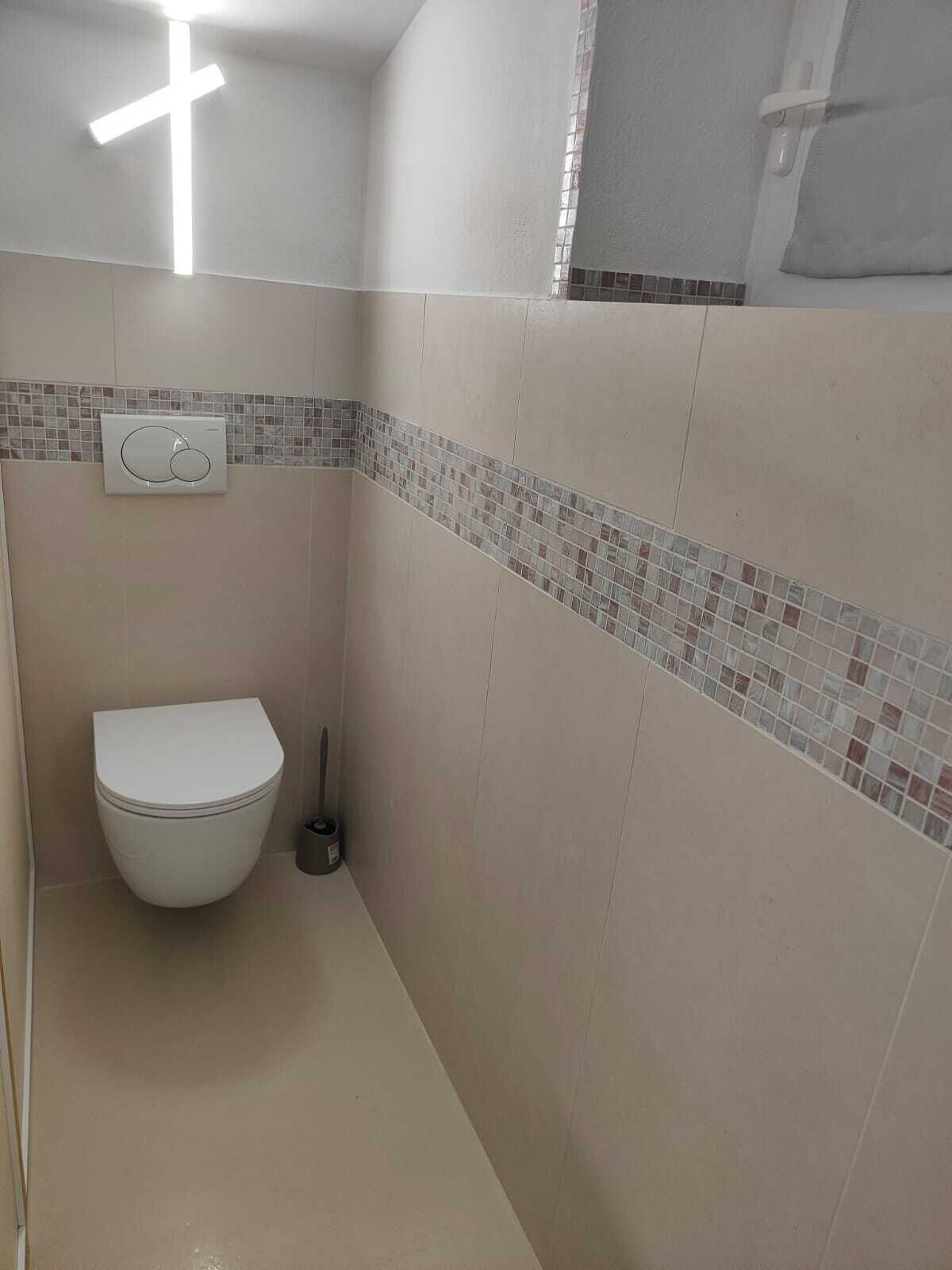 Uma casa de banho pequena e moderna, com sanita, secador de mãos e um candeeiro fixo na parede.