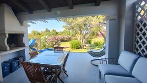 An outdoor patio with a table and chairs, a grill, and a view of a garden. - Terraced house with dehors adjacent beach in residence (San Teodoro)