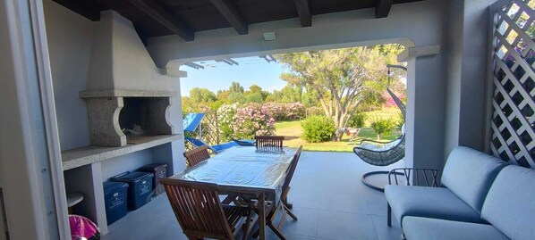 An outdoor patio with a table and chairs, a grill, and a view of a garden.