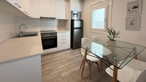 A modern kitchen with white cabinets, stainless steel appliances, a glass dining table, and a window with a view.
