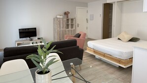 A modern, well-lit room with a flat-screen TV, a sofa, a chair, a bed, and a potted plant.