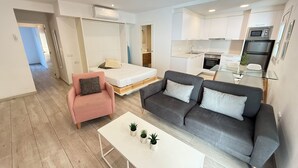 A modern apartment with a bed, sofa, coffee table, kitchenette, and a dining area.