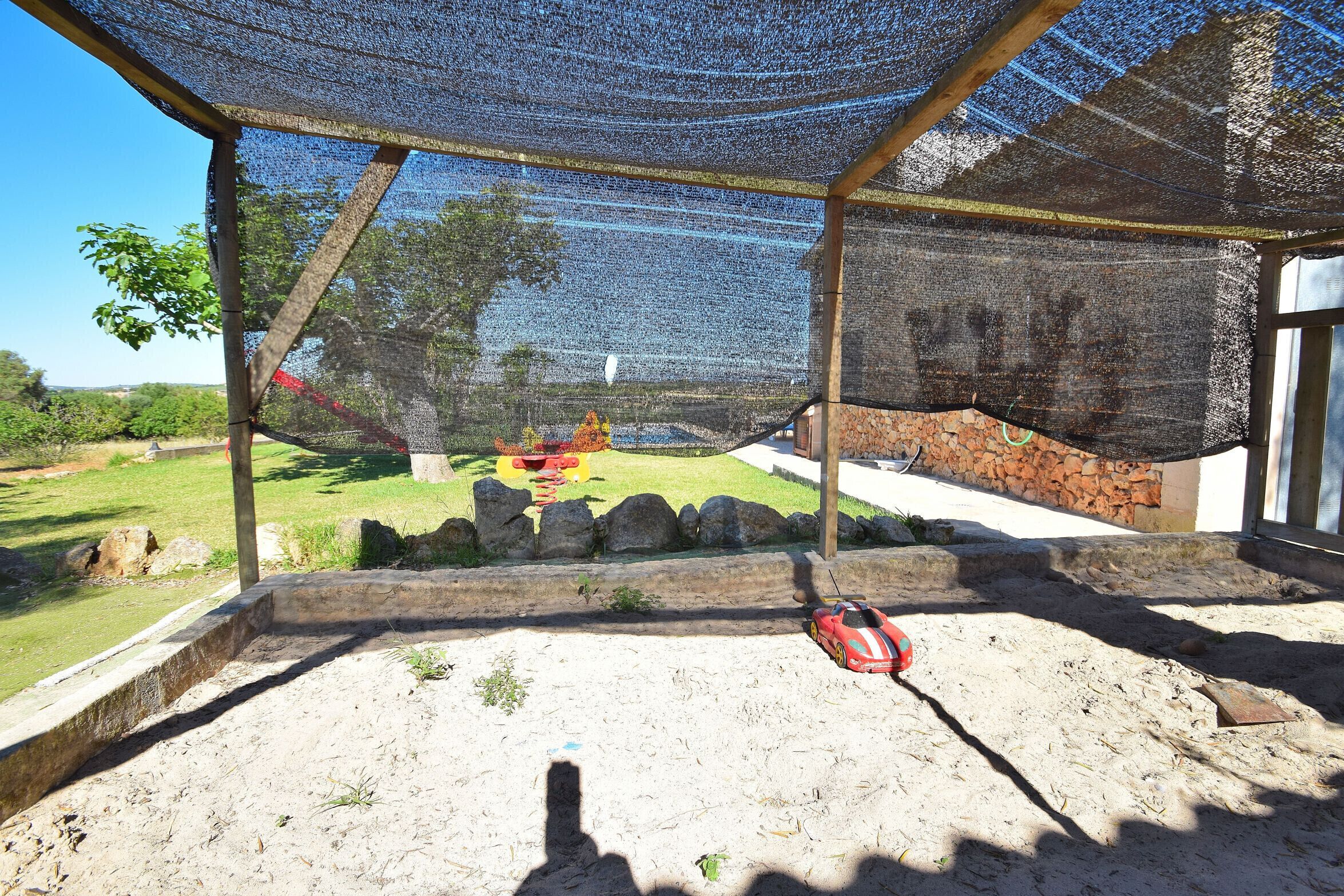 A covered outdoor area with a sandy floor, a red toy car, and a netted structure.