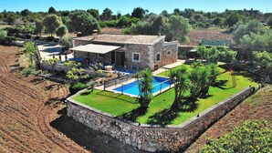 Une maison en pierre dotée d’une piscine, entourée d’un mur de pierre et d’une végétation luxuriante.