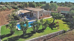Une maison en pierre avec une piscine, entourée d’une pelouse bien entretenue et d’arbres.