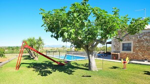 Un jardin avec une balançoire, un arbre, une maison en pierre et une piscine.