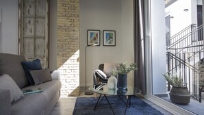 A modern living room with a grey sofa, a round glass coffee table, and a blue rug. There is a brick wall and a window with a view of a building. - Singular Stays Parque Central III (Valencia)