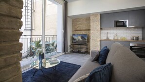 A modern kitchen with a stone accent wall, a flat-screen TV, and a dining area with a glass table and chairs. - Singular Stays Parque Central III (Valencia)