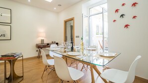 A modern dining area with a glass table, white chairs, and a view of the outdoors. - The Dreams House with Green Patio (Lisboa)