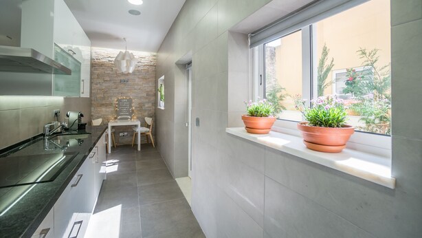 A modern kitchen with a built-in stove, a stone accent wall, and a window with potted plants. - The Dreams House with Green Patio (Lisboa)