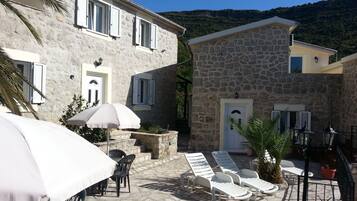 A stone building with a terrace, outdoor seating, and a view of the hills.