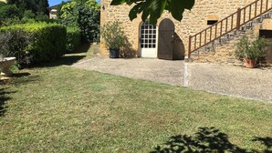 A stone building with a wooden staircase leading to a door, surrounded by a well-maintained lawn and potted plants.