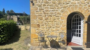 A stone building with a door, a small table, two chairs, and a garden area.