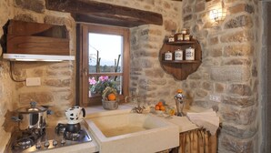 A rustic kitchen with a stone wall, wooden beams, a built-in shelf with jars, a window with flowers, and a stove. - VILLA LIZ, private pool, private hot tub, park fenced,  close to Florence (Poppi)